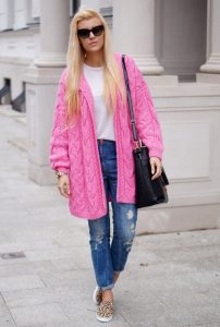 Девушка блондинка в джинсах, ярко розовом кардигане и с черной сумкой на плече